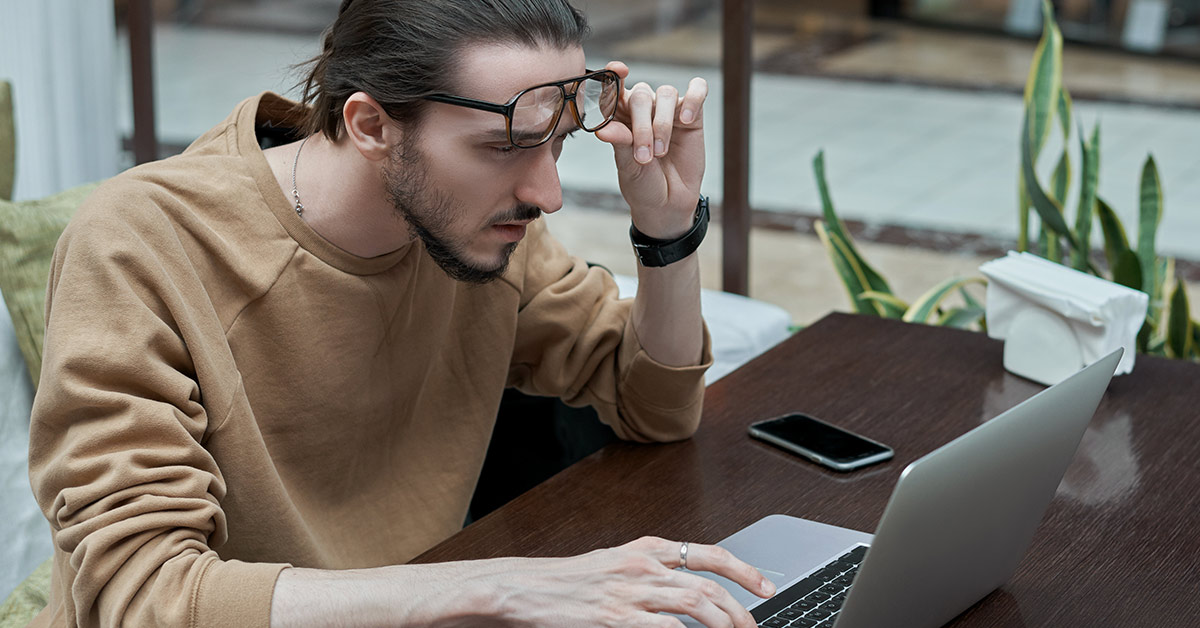 man lifting glasses while trying to focus on computer screen