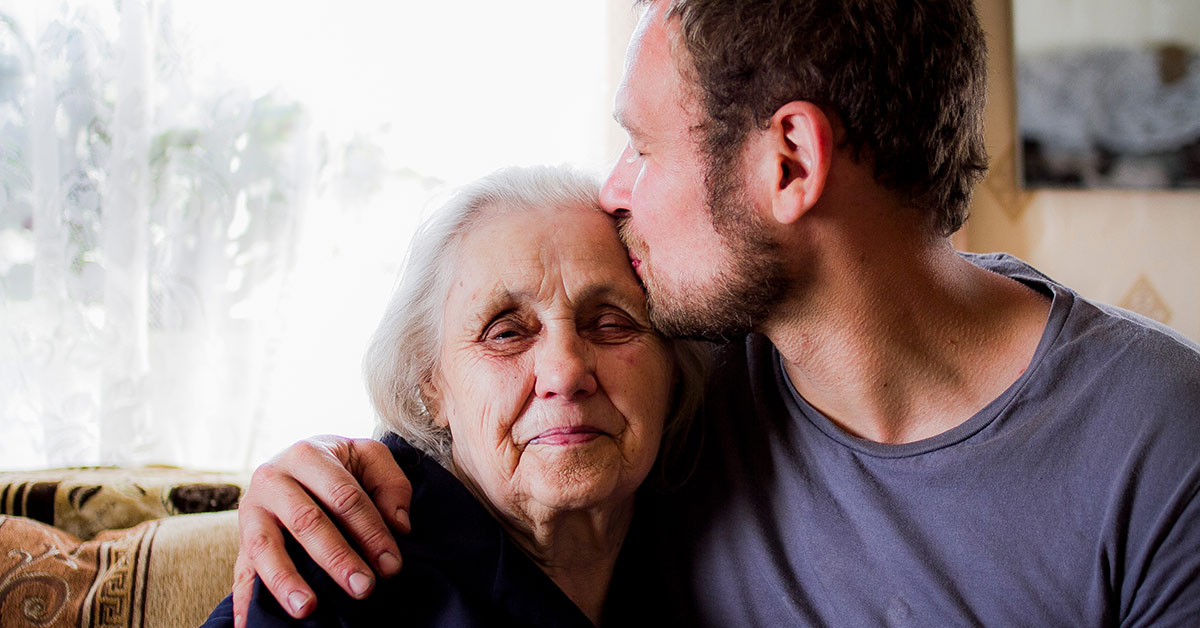 younger man kissing the forehead of elderly woman like a son to mother