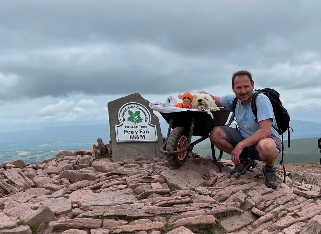 The Labradoodle on his wheelbarrow and his owner at the summit of Pen y Fan.