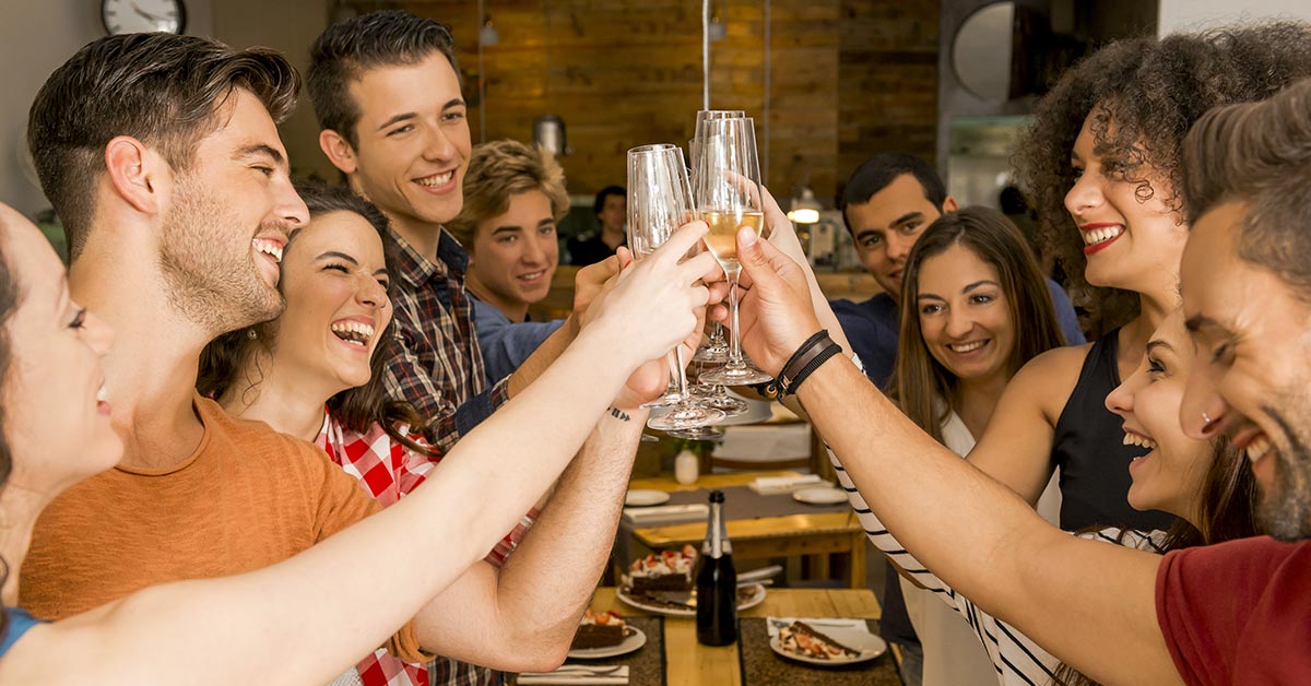 multiple friends dining at a restaurant saluting eachtother with a cheers at the table