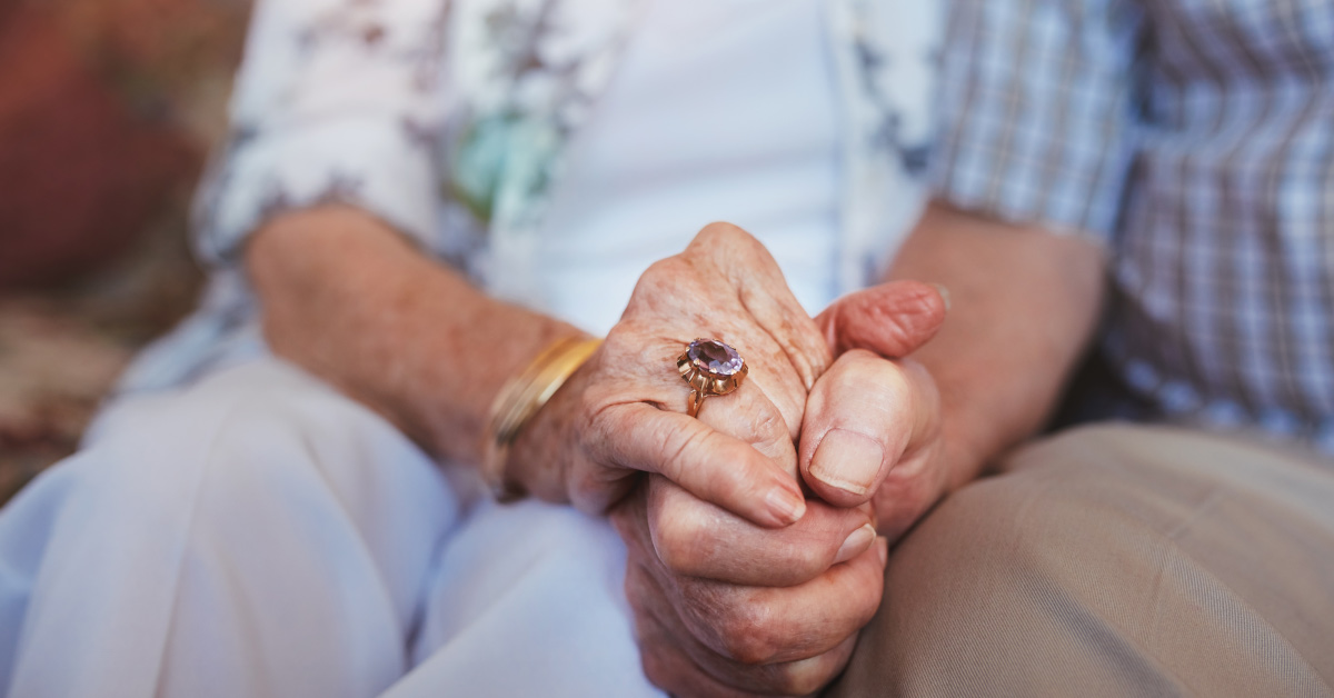 elderly married couple holding hands while sitting down