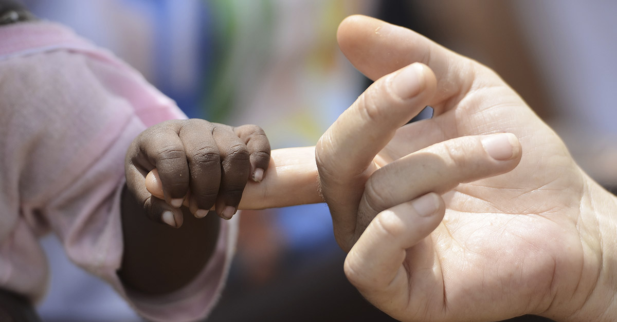 black child's hand holding a white persons finger